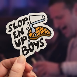 May include: White sticker with a cartoon illustration of a steak being poured on with a white pitcher. The text on the sticker reads "Slop Em Up Boys".