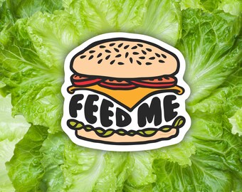 May include: A cartoon illustration of a hamburger with the text "FEED ME" on a white background. The hamburger is surrounded by green lettuce.