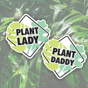 May include: Two green and white diamond-shaped stickers with the text "Plant Lady" and "Plant Daddy" in black text. The stickers have a green and white leaf design.