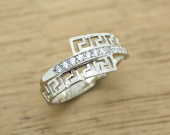 Puede incluir: Un anillo de plata con un diseño de llave griega y una fila de piedras de circonita cúbica transparentes.