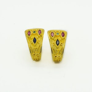 Può includere: Un paio di orecchini d'oro con un design geometrico e pietre preziose multicolori. Gli orecchini hanno la forma di una mezzaluna e presentano un motivo dettagliato.