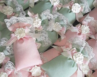 May include: A collection of small, fabric pouches with lace trim and white flower embellishments. The pouches are in shades of pink and green.