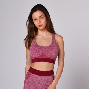 Op de afbeelding: Een vrouw draagt ​​een bordeauxrode sportbeha en leggings. De beha en leggings zijn gemaakt van naadloos, rekbaar materiaal.