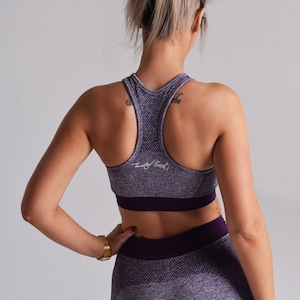 Op de afbeelding: Paarse en grijze naadloze sportbeha met een racerback-ontwerp en de tekst "Twisted Soul" gedrukt op de voorkant.