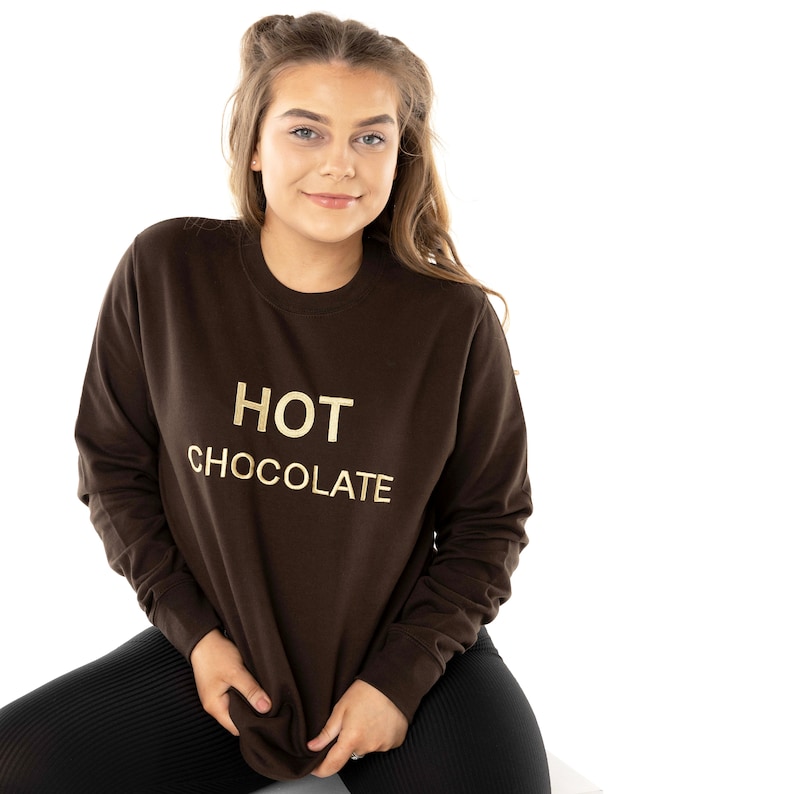 May include: A brown sweatshirt with the text "HOT CHOCOLATE" in gold lettering.