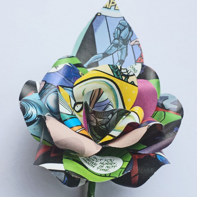 May include: A colourful paper rose made from comic book pages. The rose is green, yellow, pink, blue, and black. The text on the rose reads "But you just hurry, there is not much time."