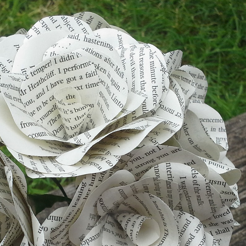 May include: A bouquet of paper flowers made from the pages of a book. The flowers are white and have a delicate, layered appearance. The text on the pages is visible, creating a unique and artistic effect.