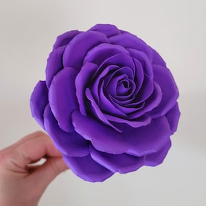 May include: A single, large, purple paper rose. The rose is made of multiple layers of paper, giving it a realistic appearance.