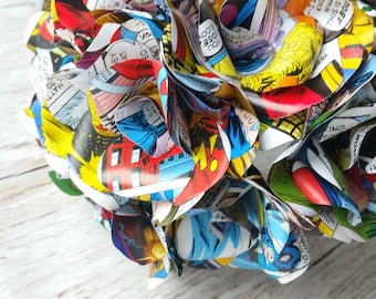 May include: A colorful bouquet of paper flowers made from comic book pages. The flowers are arranged in a circular shape and have a variety of colors, including red, blue, yellow, and green. The flowers are made from different comic book pages, and the text from the pages is visible.