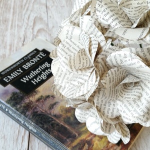 May include: A book titled "Wuthering Heights" by Emily Bront&euml;, a classic novel, is displayed with a bouquet of paper flowers made from book pages. The flowers are white and have a delicate, romantic feel.