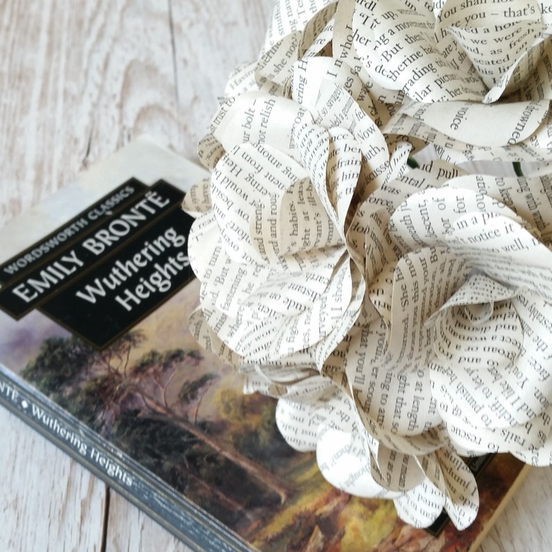 May include: A book titled "Wuthering Heights" by Emily Bront&euml;, a classic novel, is displayed with a bouquet of paper flowers made from book pages. The flowers are white and have a delicate, romantic feel.