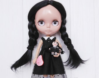 May include: A black-haired doll wearing a black and white dress and a black purse. The doll is holding a smaller doll wearing a black and white dress. The doll has a black and white checked skirt and white socks.