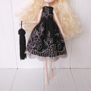 May include: A black dress with silver floral embroidery and a lace trim. The dress is being worn by a doll with blonde hair.