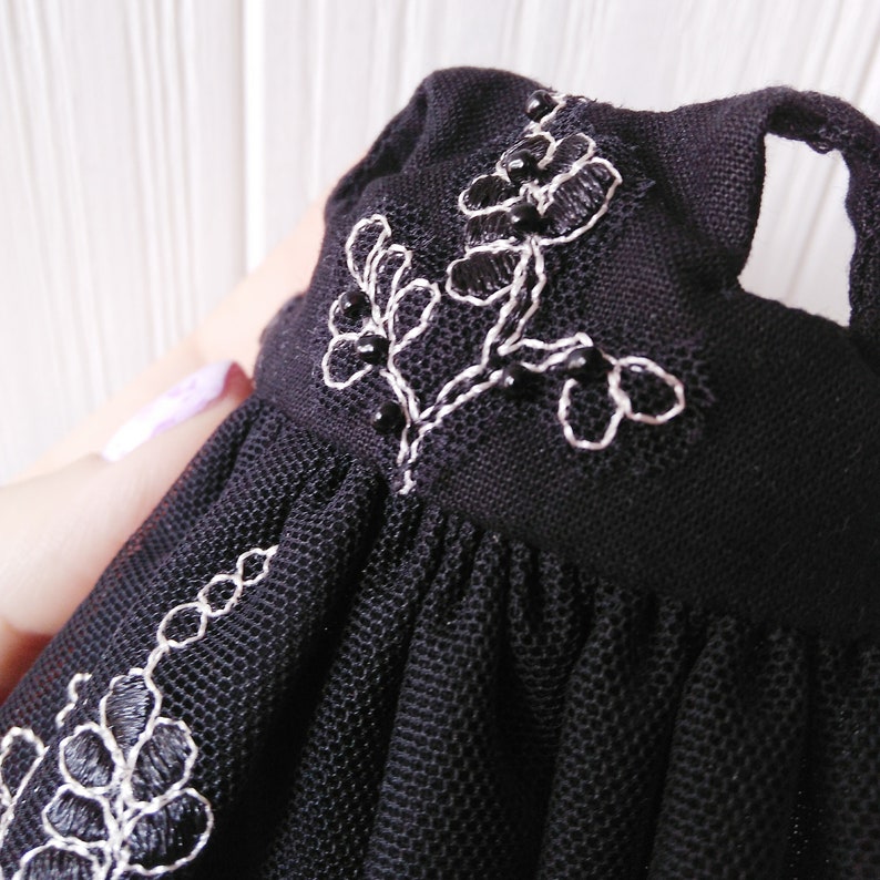 May include: Black tulle dress with white and black floral embroidery. The dress has a fitted bodice and a full skirt.