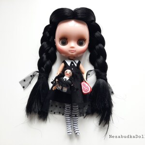 May include: A black haired doll with a black and white dress and black and white striped stockings. The doll is holding a smaller doll in a similar outfit. The doll is wearing a necklace with a small red meat charm.