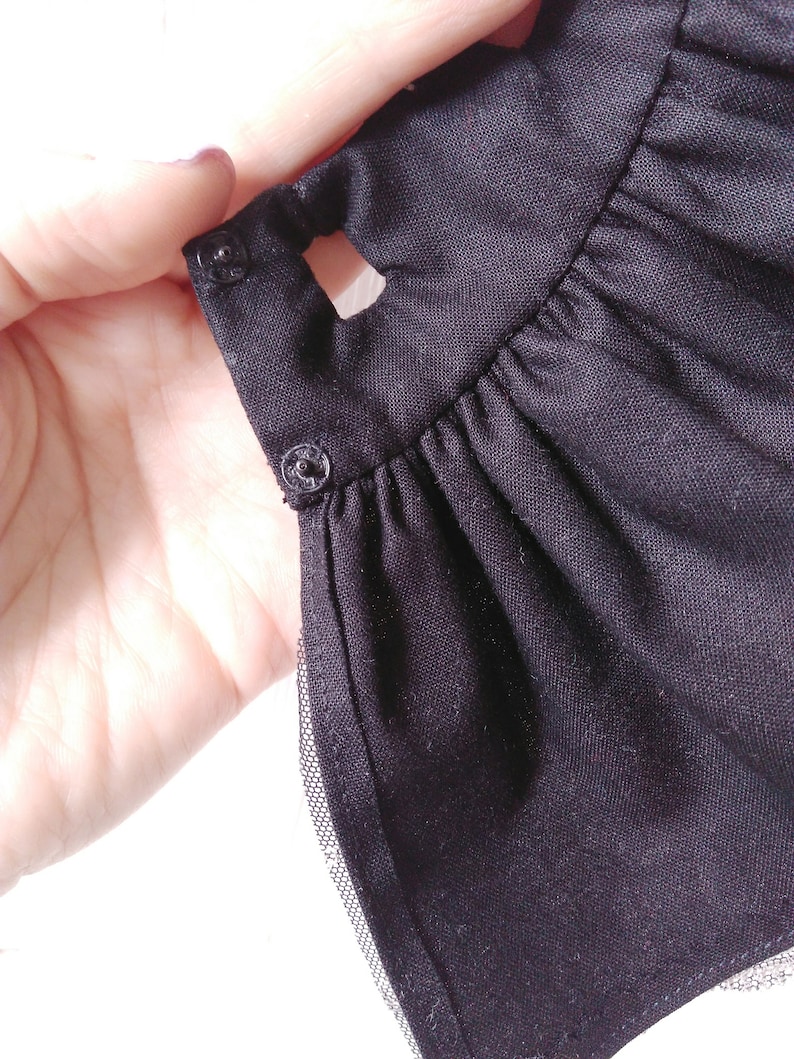 May include: Black dress with a ruffled hem and a black tulle overlay. The dress has two black buttons on the side.