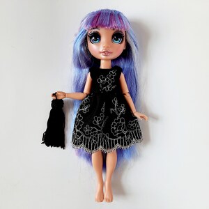 May include: A doll with long, blue and purple hair wearing a black dress with silver embroidery and holding a black tassel.