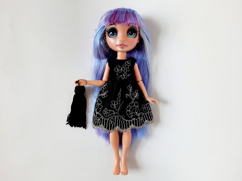 May include: A doll with long, blue and purple hair wearing a black dress with silver embroidery and holding a black tassel.