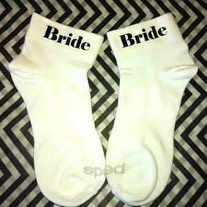 May include: A pair of white ankle socks with the word "Bride" printed in black on each sock.
