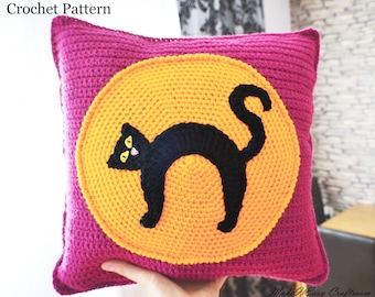 May include: A crocheted pillow with a black cat silhouette on a yellow circle in the center. The pillow is a deep pink color.