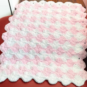 May include: A pink and white crocheted baby blanket with a scalloped edge.