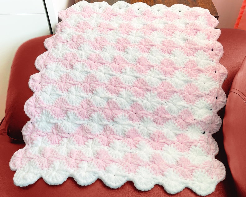 May include: A pink and white crocheted baby blanket with a scalloped edge.