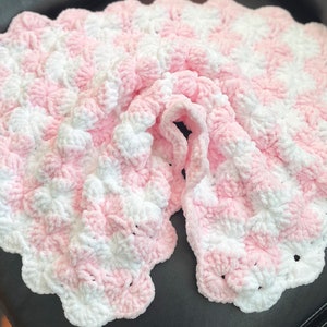 May include: A pink and white crocheted baby blanket with a textured, puffy design.