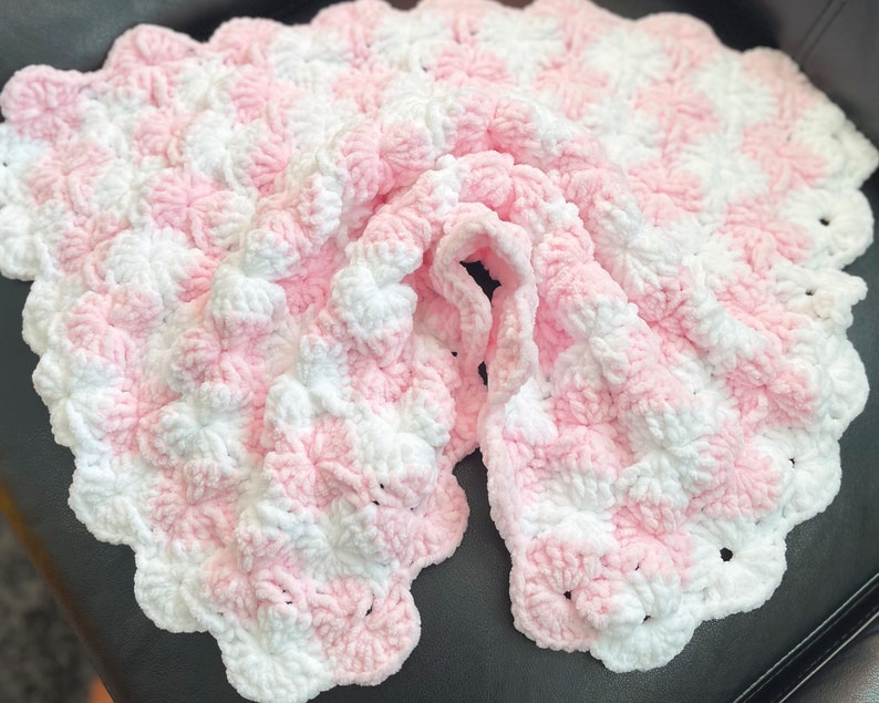 May include: A pink and white crocheted baby blanket with a textured, puffy design.