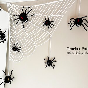 May include: A white crocheted spider web with eight black crocheted spiders hanging from it. The web is hanging in a corner of a white wall. The text "Crochet Pattern Make It Easy Craftroom" is in the bottom right corner of the image.