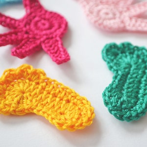 Puede incluir: Cinco formas de ganchillo en diferentes colores: amarillo, rosa, verde y azul. Las formas son una mano, un pie y otras dos formas abstractas.