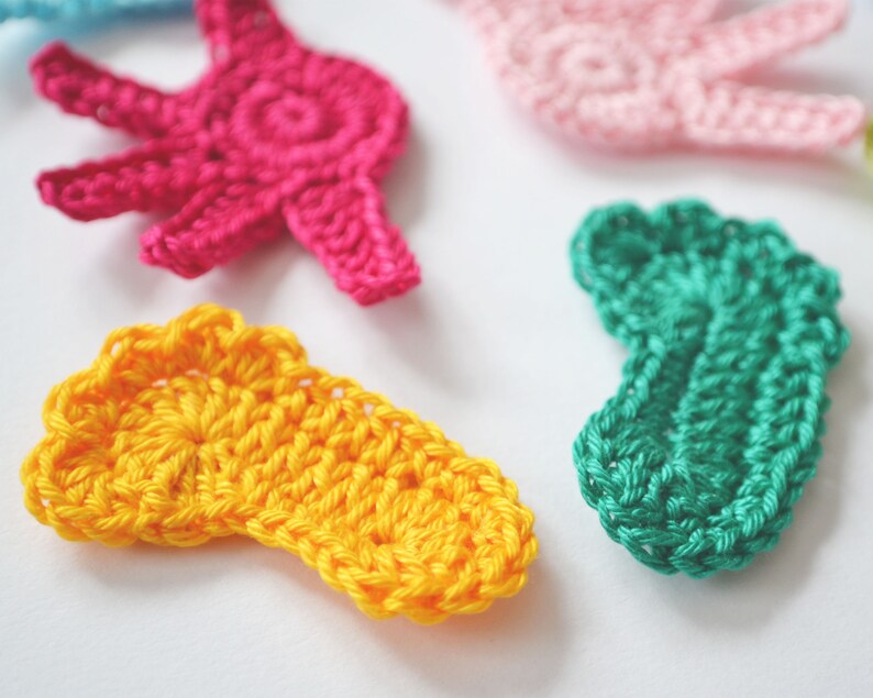 Puede incluir: Cinco formas de ganchillo en diferentes colores: amarillo, rosa, verde y azul. Las formas son una mano, un pie y otras dos formas abstractas.
