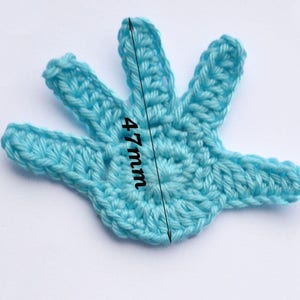 Puede incluir: Una aplicaci&oacute;n de mano de ganchillo de color azul claro que mide 12 cm de largo. La mano tiene cinco dedos y un centro detallado.