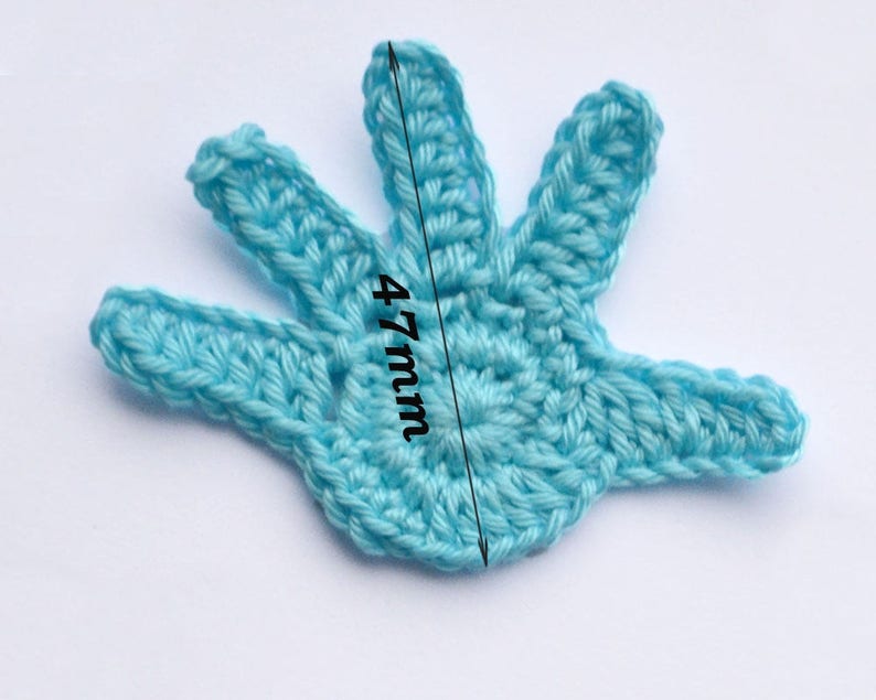 Puede incluir: Una aplicaci&oacute;n de mano de ganchillo de color azul claro que mide 12 cm de largo. La mano tiene cinco dedos y un centro detallado.