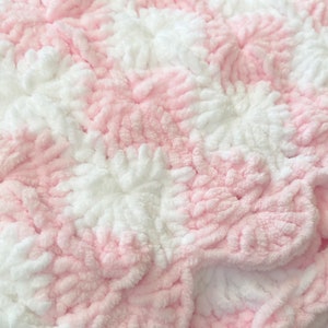 May include: Pink and white crocheted baby blanket with a textured, fluffy design.