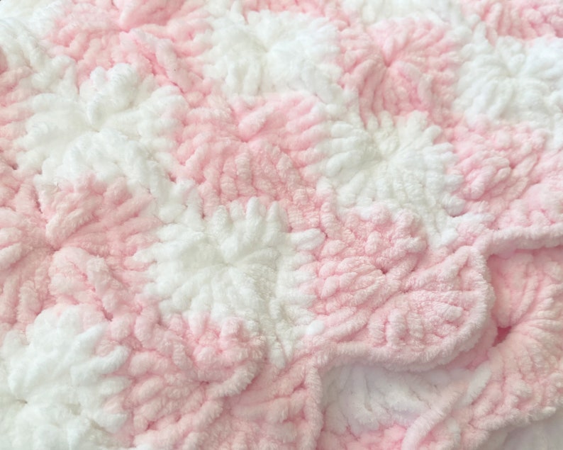 May include: Pink and white crocheted baby blanket with a textured, fluffy design.