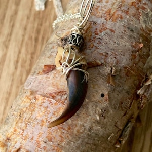 May include: A silver chain necklace with a pendant featuring a brown animal claw wrapped in silver wire and a silver bead with an ornate design.