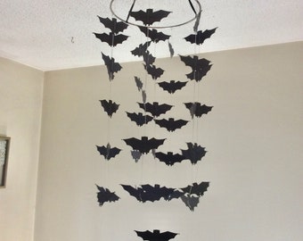 May include: A black bat mobile hanging from a silver ring. The bats are suspended from strings of varying lengths, creating a cascading effect. The mobile is a fun and festive decoration for Halloween.