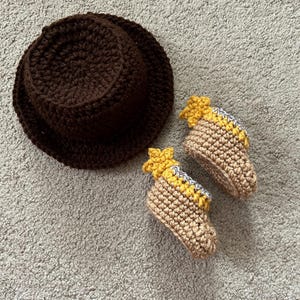 May include: A brown crocheted hat and a pair of tan crocheted baby booties with yellow star accents.