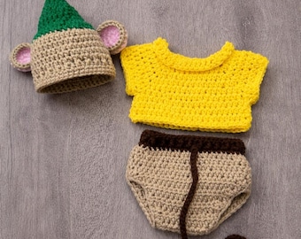 May include: A handmade crochet baby outfit in a monkey theme. The set includes a yellow shirt, tan diaper cover with a brown drawstring, and a tan hat with green top and pink ears.