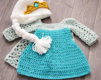 May include: A crochet baby outfit in a princess theme. The set includes a turquoise dress, a light green top with sleeves, and a white hat with a gold crown and a long white braid. The outfit is handmade.