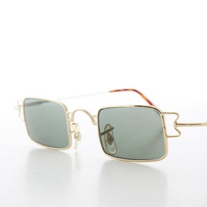 Puede incluir: Gafas de sol de metal dorado con lentes cuadradas verdes. Las gafas tienen un diseño único con un pequeño acento metálico en el lateral de la montura.