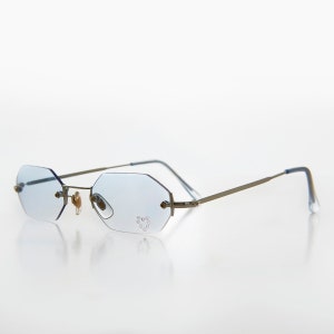 May include: Silver rimless octagon shaped sunglasses with light blue lenses and a small heart design of rhinestones on the right lens.
