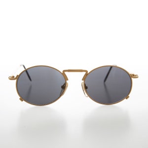Puede incluir: Gafas de sol redondas de metal dorado con lentes negros. Las gafas tienen un fino marco de metal y están diseñadas para ser usadas en la cara.