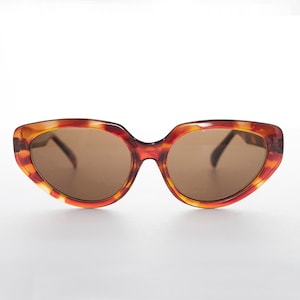 Könnte beinhalten: Eine Sonnenbrille im Cat-Eye-Stil aus braunem und orangefarbenem Schildpatt mit braunen Gläsern.