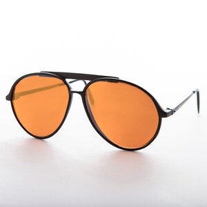K&ouml;nnte beinhalten: Schwarze Aviator-Sonnenbrille mit orangenen Gl&auml;sern und einem Metallrahmen.