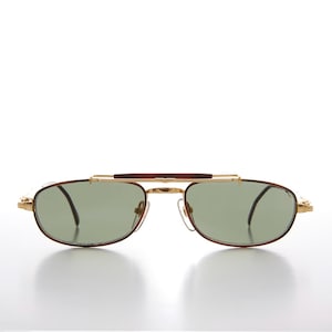 Puede incluir: Gafas de sol doradas con barra superior y patillas marrones. Las lentes ovaladas son verdes. Las gafas tienen doble puente y un diseño clásico y vintage.
