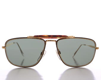 May include: Gold-tone aviator sunglasses with brown tortoise shell accents on the bridge and arms. The lenses are green and have a slight tint.