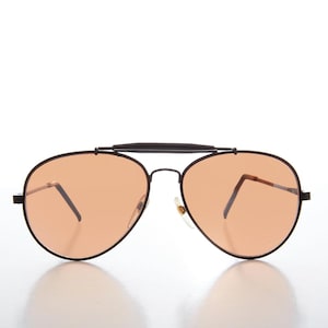 Op de afbeelding: Aviator zonnebril met een zwart metalen montuur en oranje getinte glazen. De zonnebril heeft een dubbele brug en een wenkbrauwstang. De pootjes zijn dun en licht gebogen. De glazen zijn druppelvormig.