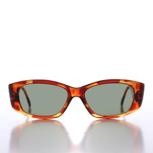 May include: Rectangular sunglasses with a tortoiseshell pattern frame and gray lenses. The sunglasses have a classic design, suitable for various face shapes. The frame features a blend of brown and amber hues.