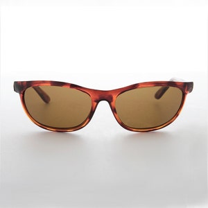 Könnte beinhalten: Sonnenbrille mit Schildpattrahmen und braunen Gläsern. Die Sonnenbrille hat eine klassische, rechteckige Form mit leicht geschwungener Oberseite. Die Gläser sind warmbraun und der Rahmen hat ein gesprenkeltes Braun- und Bernsteinmuster.